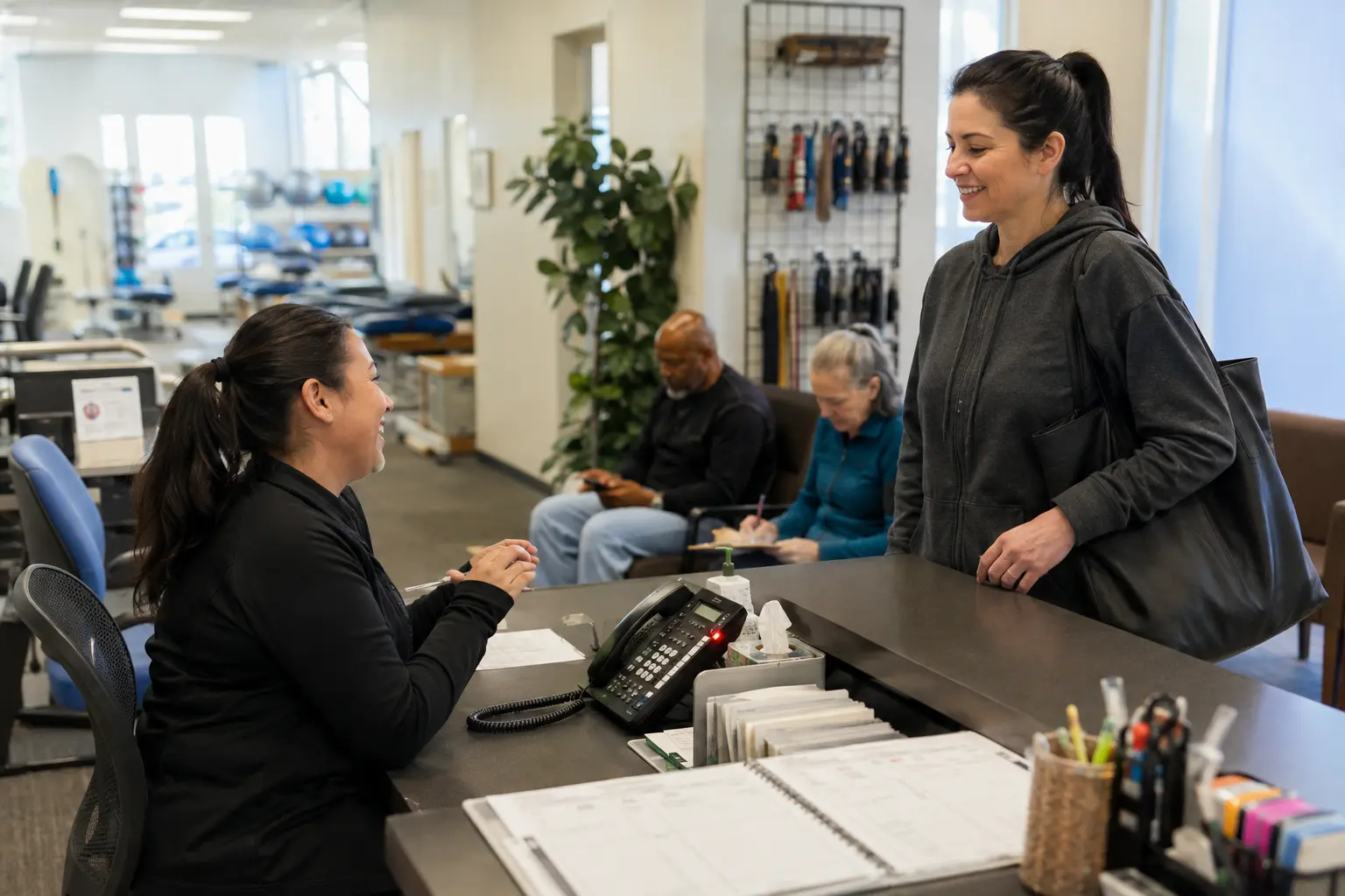 A physical therapy clinic receptionist welcoming a patient while calls and appointments require attention